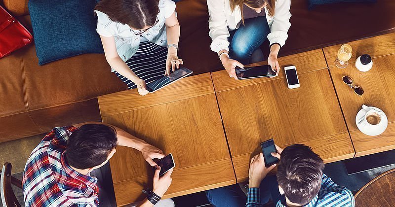 Junge Menschen mit Tablets und Smartphones an einem Holztisch
