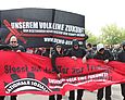Schwarz gekleidete Personen tragen ein rotes Banner, auf dem der Schriftzug "Stoßt auf das Tor zur Freiheit" zu lesen ist.