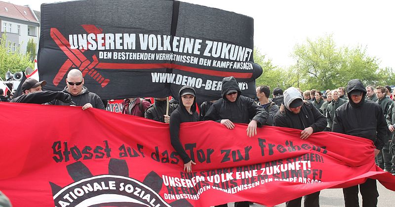 Schwarz gekleidete Personen tragen ein rotes Banner, auf dem der Schriftzug "Stoßt auf das Tor zur Freiheit" zu lesen ist.