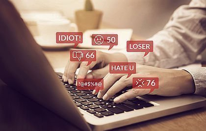 Hände auf Tastatur mit eingeblendeten Hatespeech-Nachrichten