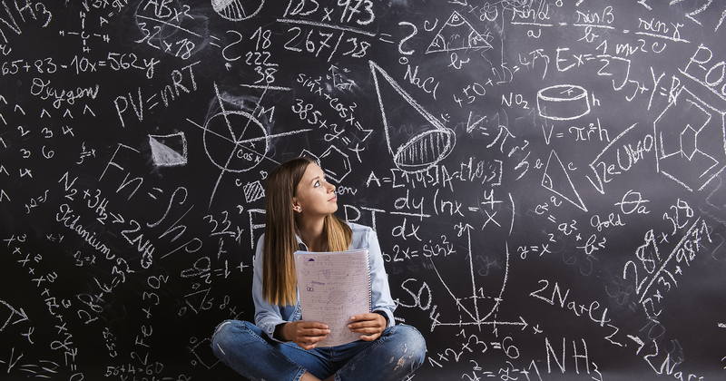 Mädchen sitzt vor bunt bemalter Tafel mit Mathe-Aufgaben und -Formeln