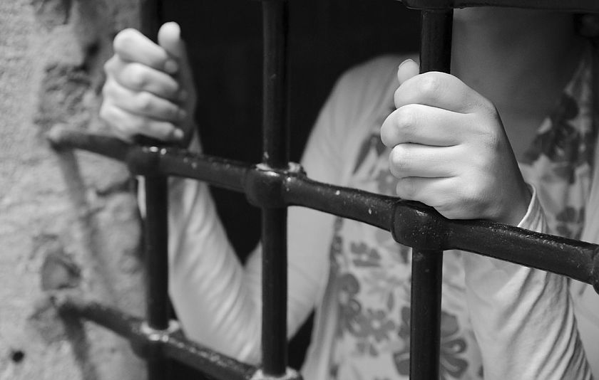 Oberkörper einer Frau, die sich an Gitterstäben festhält.