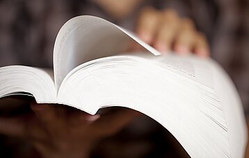 In einem dicken Buch wird eine Seite umgeblättert.
