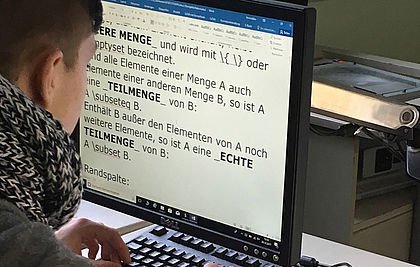 Sehbehinderter Schüler arbeitet vor dem PC mit einem digitalisierten Heft für Mathematik.