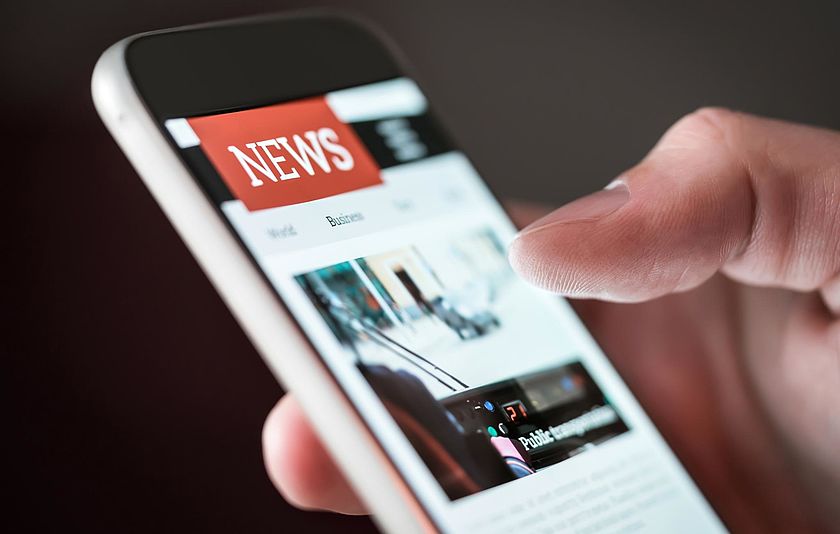 Newsmeldung auf Smartphone Man sieht, eine Hand mit einem Smartphone in der Hand, auf dem eine Nachrichten-App geöffnet ist.