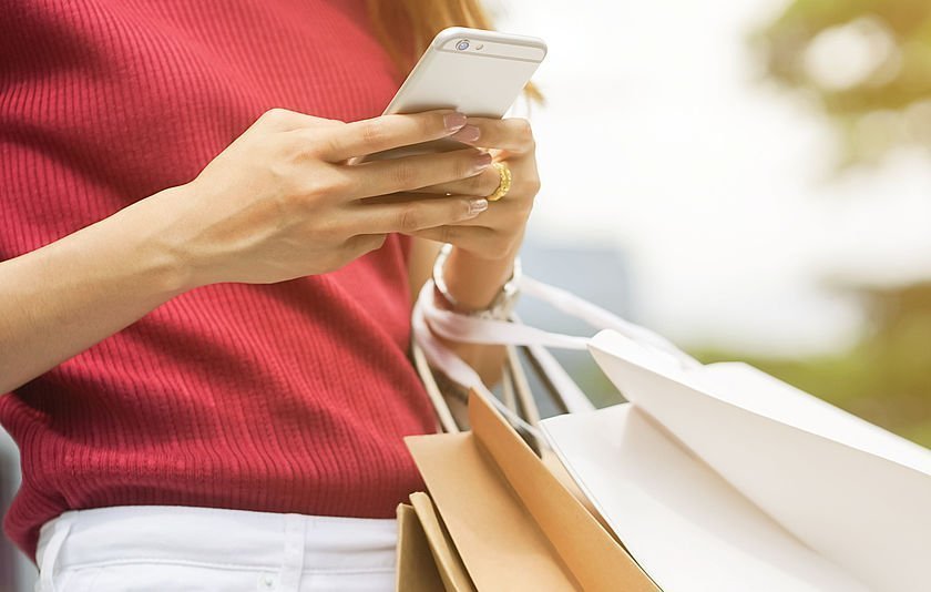 Person mit Handy in den Händen und Shopping-Taschen