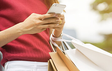 Person mit Handy in den Händen und Shopping-Taschen
