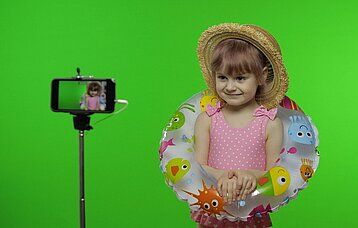Kleines Mädchen mit Badesachen steht vor einem Greenscreen bei einem Fototermin.