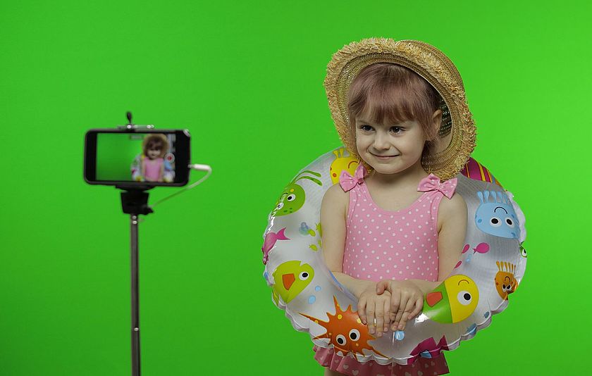 Kleines Mädchen mit Badesachen steht vor einem Greenscreen bei einem Fototermin.