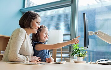 Frau mit kleinem Kind vor einem PC-Bildschirm