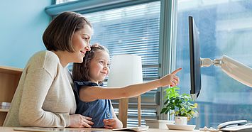 Frau mit kleinem Kind vor einem PC-Bildschirm