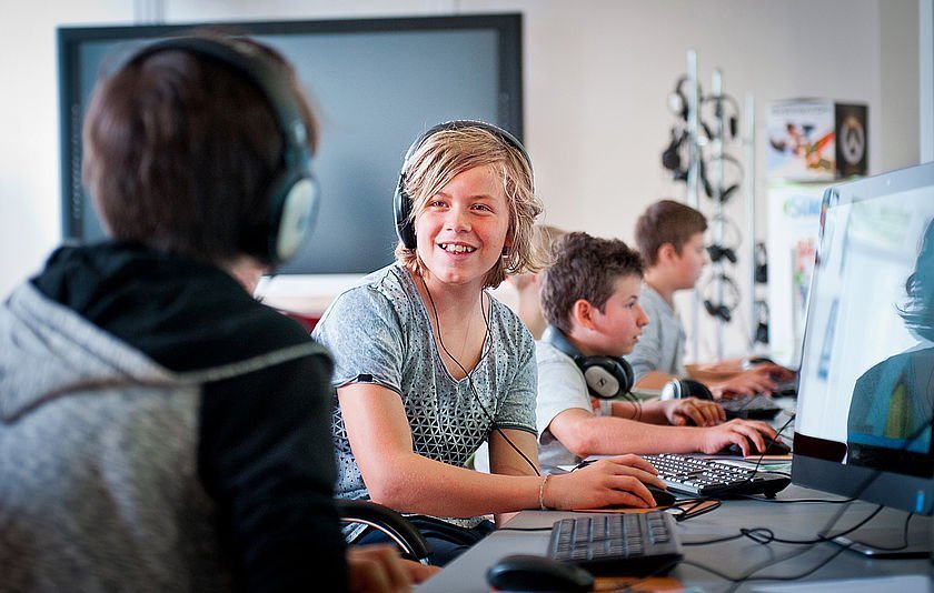 Schülerinnen und Schüler sitzen in einem Raum vor PCs