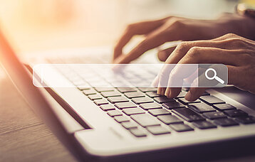 Hände auf Laptop-Tastatur und eingeblendetes Suchfeld