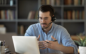 Mann im Home Office mit Headset am Notebook im Gespräch.