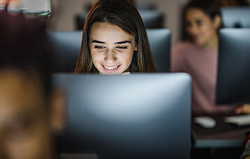 Lächelnde Schülerin vor ihrem PC in einer Computerklasse.