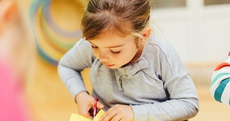 Mädchen schneidet mit Schere in Papier