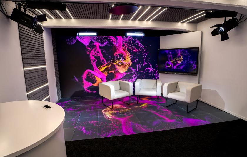 LMZ Studio Drei hellgraue Sessel stehen auf einem gekachelten LED-Boden vor einer LED-Wand, die in einer pink-lila Grafik erstrahlen.