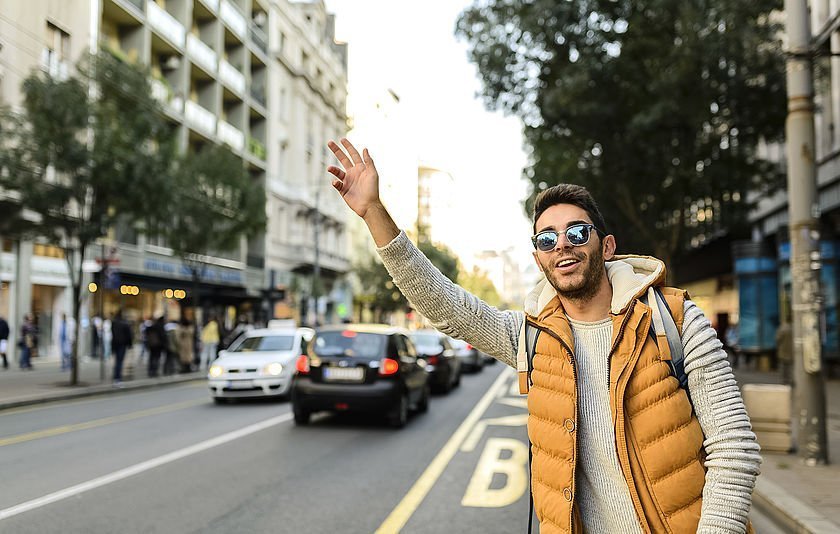 Junger Mann am Straßenrand winkt einem Taxi