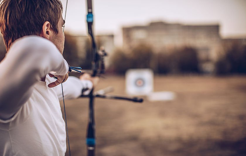 Mann schhießt mit Armbrust auf eine Zielschreibe Mann schhießt mit Armbrust auf eine Zielschreibe