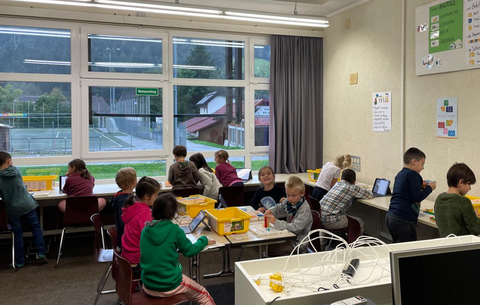 Das Klassengeschehen in einer ersten Klasse während der Robotik-Stunde an der Grundschule Simonswald. Die Kinder arbeiten selbsständig in Zweiergruppen und wirken engagiert und eifrig.