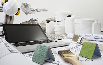 Das Foto zeigt ein Notebook und etliche Gerätschaften wie wie Pinsel und Farbeimer.