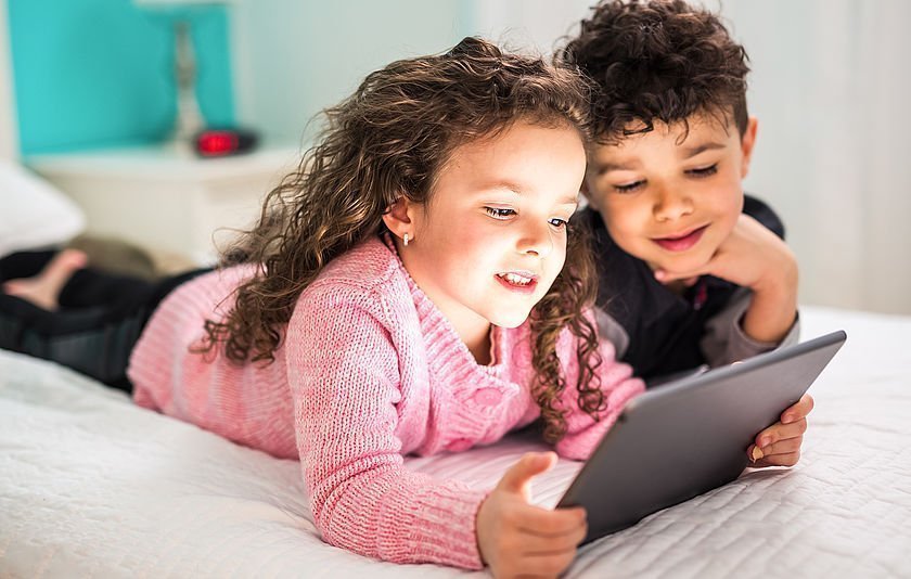 Kinder mit Tablet liegen auf einem Bett Kinder mit Tablet liegen auf einem Bett