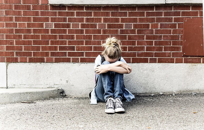 Mädchen sitzt zusammengekauert vor einer Mauer