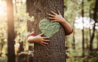Baumstamm mit einem Herzen aus Moos, der von einem kleinen Jungen umarmt wird.