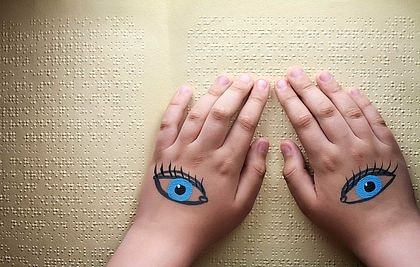 Hände mit aufgemalten Augen liegen auf Seiten mit Braille-Schrift