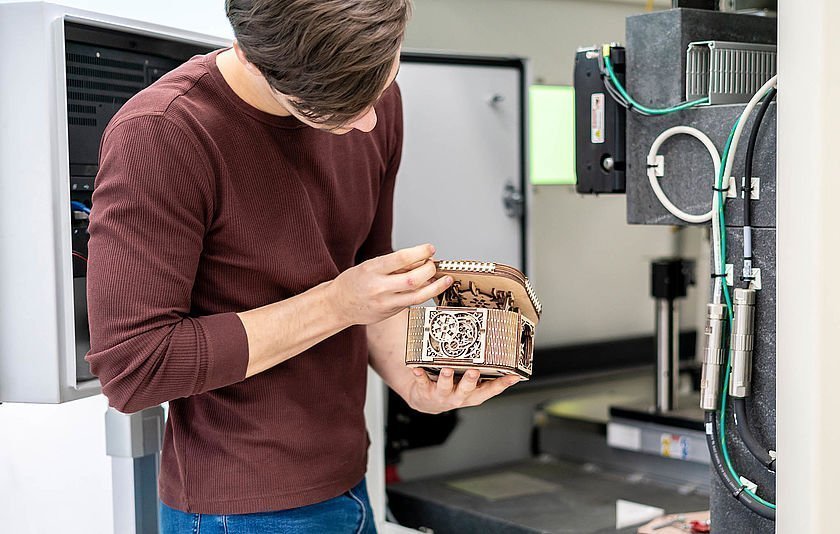 Schüler mit Holzbox vor einem Laser-Cutter