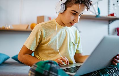 Ein Schüler sitzt mit Kopfhörern vor einem Laptop.