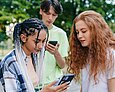 Zwei Teenager-Mädchen und ein Teenager-Junge schauen auf ihre Handys.
