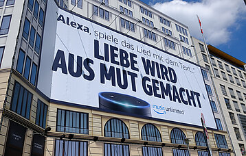 Produktwerbung Alexa, Plakat an einer Hauswand mit dem Schriftzug Liebe wird aus Mut gemacht