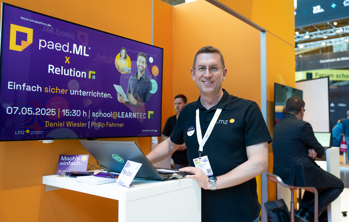 Mann in schwarzem LMZ-Polo-T-Shirt steht vor einem lila beleuchteten Display am Messestand