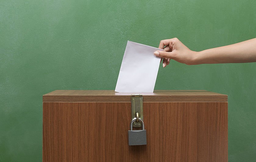 Hand steckt Zettel in eine Wahlurne Hand steckt Zettel in eine Wahlurne