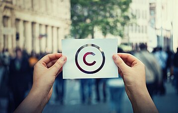 Zwei Hände halten ein Blatt Papier mit dem Copyright-Zeichen in die Höhe. 