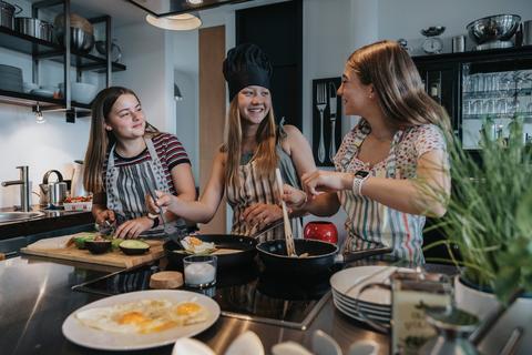 Drei junge Mädchen im Teenager-Alter in einer modernen Küche beim Kochen
