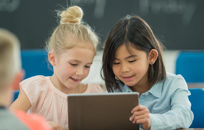 Zwei Grundschülerinnen schauen auf ein Tablet