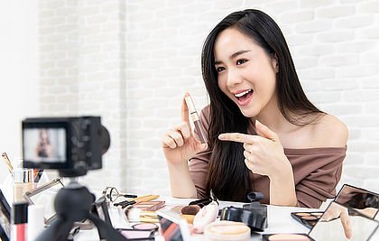 Junge Frau mit Kosmetik-Artikeln vor einer Kamera