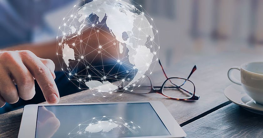 Hand über einem Tablet mit eingeblendetem Globus, um ein Globales Netzwerk zu simulieren.