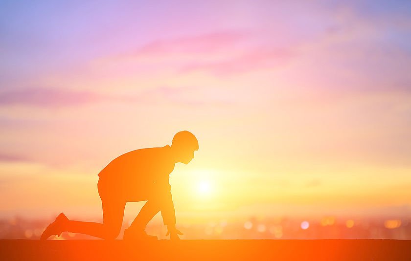 Mann kniet am Rennstart. Mann kniet am Rennstart. Im Hintergrund Abendrot.