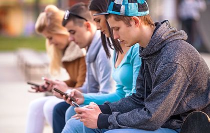 Vier Teenager sitzen auf einer Bank und schauen auf ihr Smartphone.
