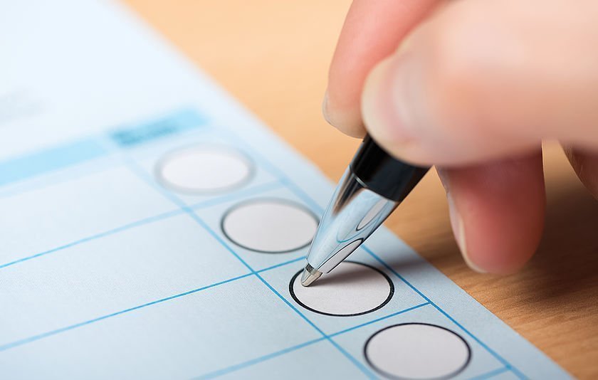 Hand mit Kugelschreiber beim Ankreuzen eines Wahlzettels