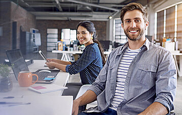 Mann und Frau an einem Schreibtisch mit Laptop und Tablet