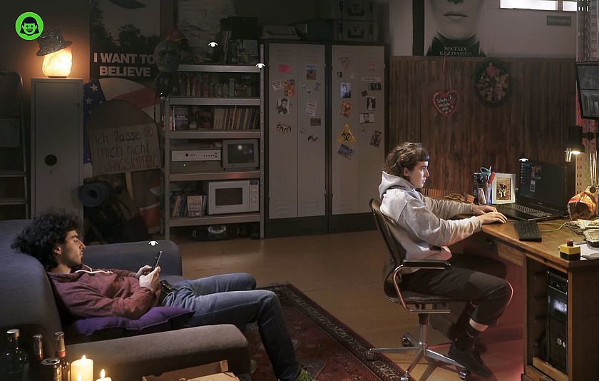 Jugendliche vor dem PC am Schreibtisch und ein Jugendlicher auf dem Sofa mit dem Handy.