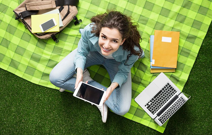 Junge Frau mit Laptop und Tablet auf einer Picknickdecke