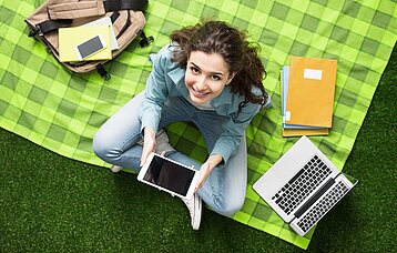 Junge Frau mit Laptop und Tablet auf einer Picknickdecke
