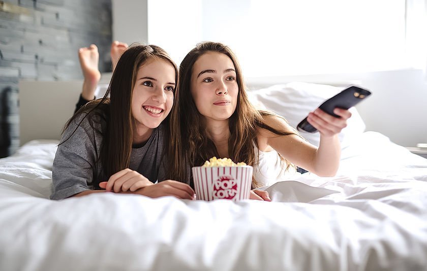 Zwei Mädchen liegen auf dem Bett mit einer Fernbedienung in der Hand