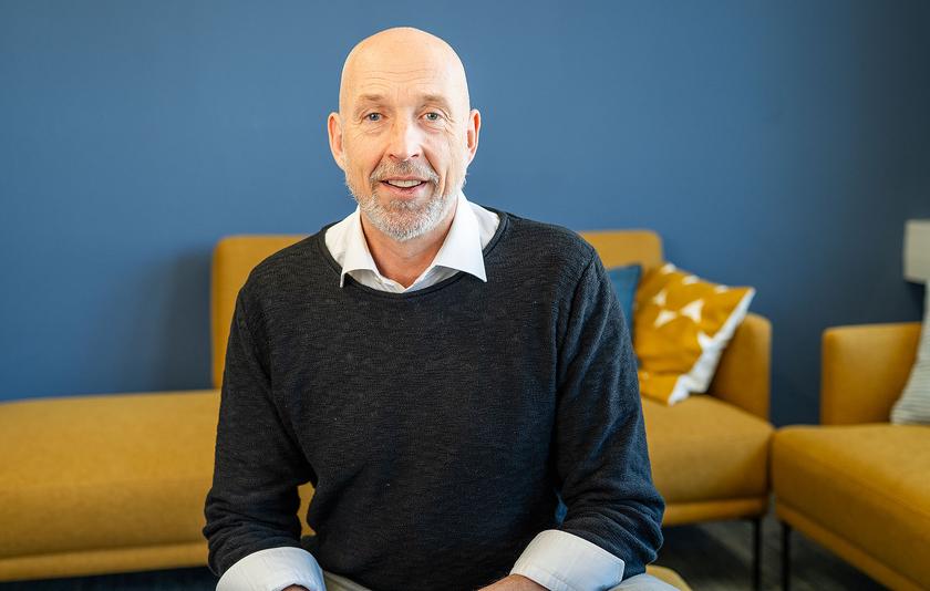 Ulrich Hollritt, Mitarbeiter des LMZ, sitzt vor gelbem Sofa und blauer Wand.