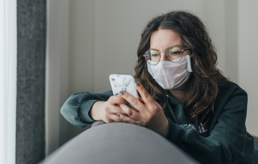 Frau mit Mundschutz liest Nachrichten auf dem Smartphone
